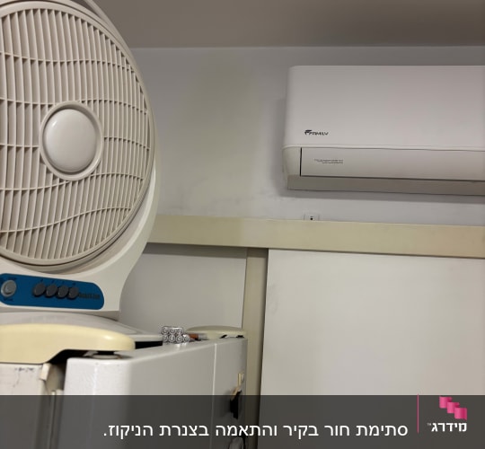 מזגן עילי מותקן על קיר ומאוורר נייד על מקרר
